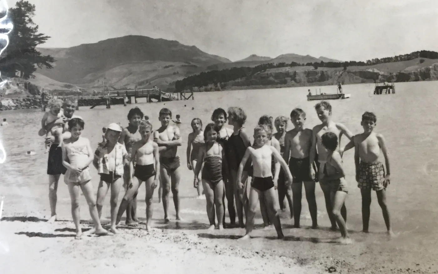 Old black and white photo of a group of children in swimsuits on a beach, with hills behind