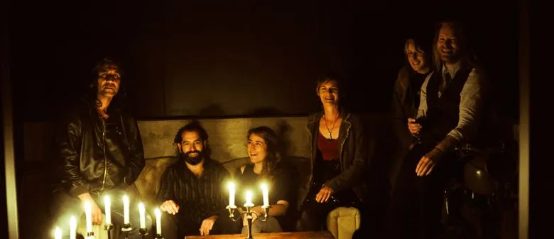 A group of people sit together in a dark room lit by candles